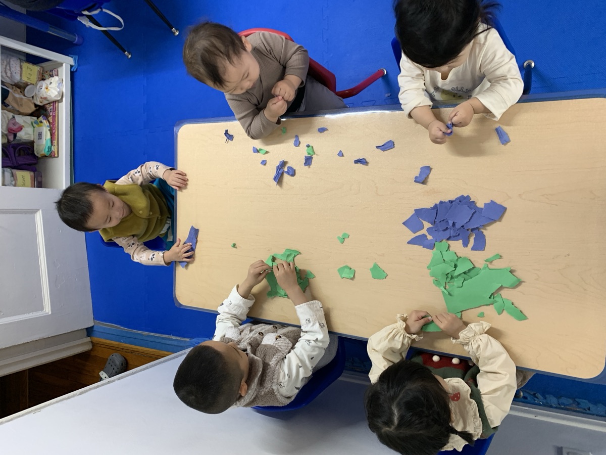 五位小朋友围坐桌边一起玩蓝绿色彩泥撕贴手工