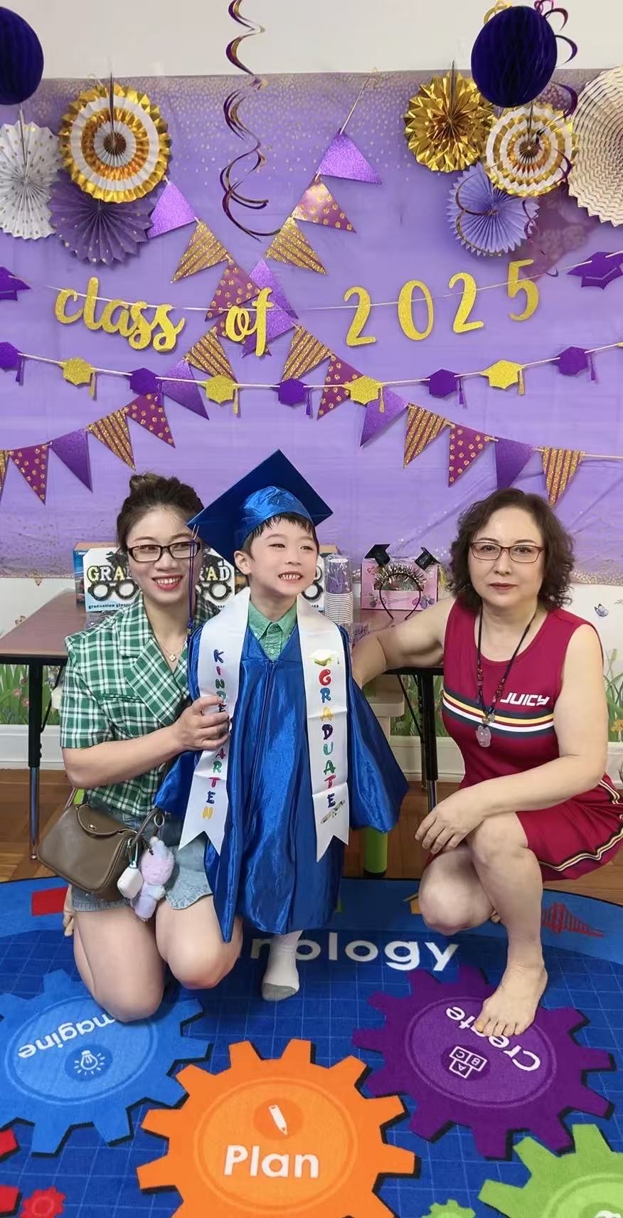 2025届毕业小朋友身穿蓝色学士服与老师在Class of 2025背景墙前合影