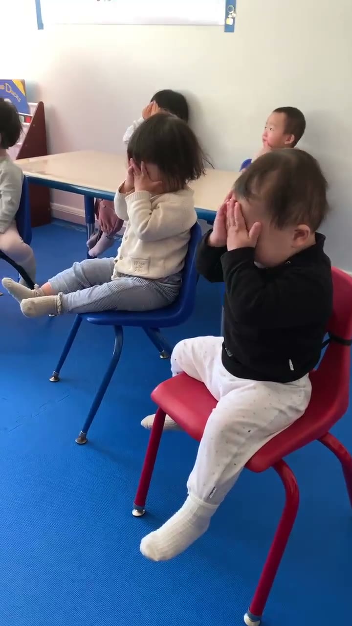 孩子们坐在小椅子上做遮脸躲猫猫互动游戏